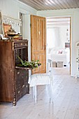 Rustic chair at vintage bureau in front of open door with view into living room