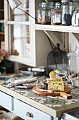Detail of kitchen counter, cheese on wooden board, storage jars on bracket shelves