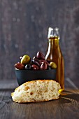 A slice of unleavened bread, olives and a bottle of olive oil