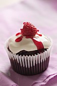 A chocolate and raspberry cupcake topped with cream, raspberry syrup and a fresh raspberry