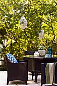 Dunkle moderne Outdoorsessel mit Tisch auf Terrassenplatz im Garten einer alten Villa mit an Bäumen hängenden Laternen