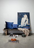 Hand-dyed indigo cushions and nude painting of woman on bamboo couch with fabric seat behind plexiglas side table