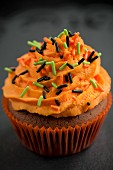 A chocolate cupcake with orange buttercream and sugar sprinkles for Halloween
