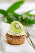 A cupcake topped with cream and a slice of kiwi