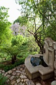 Concrete fountain against stone wall in woodland-style garden