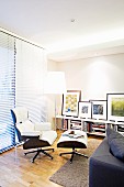 Classic, designer lounge chair and footstool in front of floor-to-ceiling louver blinds in modern living room