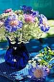 Cobalt blue glass vase of violet scabious and cow parsley on blue fabric with white polka dots