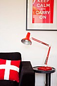 Rotweisse Accessoires zu schwarzem Sofa - Kissen mit Schweizer Fahne und gerahmtes Bild mit Sinnspruch über Beistelltisch und Leselampe