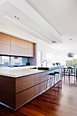 Designerküche in lichtdurchflutetem Wohnraum; lange Theke mit Holzfront und aufgesetzter Platte für Frühstücksbar
