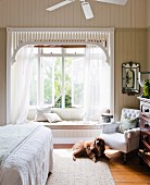 Dog in front of armchair in bedroom; romantic bay window with curtains and integrated window seat