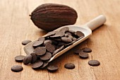 Cooking chocolate buttons on a wooden scoop with a cocoa pod in the background