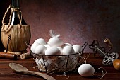 Fresh eggs in a wire basket next to antique kitchen utensils and a bottle of wine