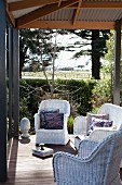 weiße Rattansessel auf überdachter Terrasse mit Vintageflair, Blick über sonnigen Garten in ländliche Umgebung