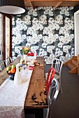 Red and white chairs at rustic wooden table in front of wall covered in floral wallpaper