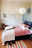 Double bed with red and white striped bed linen against partition and white wooden wall in background in rustic, modern bedroom