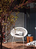 Retro shell chair and stool on wooden terrace with concrete-block wall and dark glass wall in background