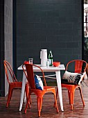 Orange vintage chairs and white table on wooden terrace against grey concrete-block wall of designer house