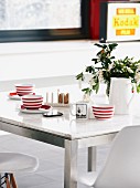 Rot-weiss gestreifte Tassen auf Esstisch mit Marmorplatte und Metallgestell, dazu klassische Schalenstühle von Eames