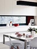 Red and white striped cups on dining table with marble top and metal frame combined with classic Eames chairs in front of fitted kitchen