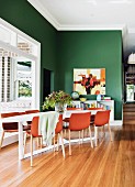 Red-brown shell chairs around table in corner next to window in front of green-painted wall in open-plan dining area