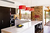 White counter-style table below red pendant lamps in contemporary kitchen area