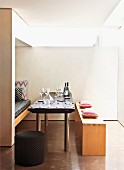 Wine glasses on table between simple wooden bench and fitted bench in niche with seat cushion in minimalist dining area