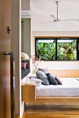 View through open door of stacked pillows on floating modern bed and palm trees seen through open window