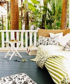 Oase in tropischem Ambiente, gemütliche Rattan Tagesliege mit Kissen und Decken auf Veranda