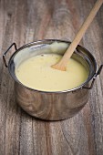 Homemade vanilla pudding in a pan with a wooden spoon