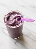 A blueberry smoothie made with soy milk in a glass with a spoon