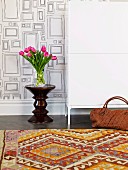 Tulpenstrauss und Designer Hocker vor Wandgestaltung mit Rechteckmuster; traditionell gemusterter Kelim im Vordergrund