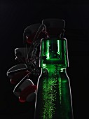 A green beer bottle with a flip-top lid backlit against a black background being opened (multiple expose)
