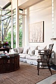 Traditional wooden armchair next to white couch and books stacked on low table in modern living room with glass extension