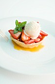 A strawberry tartlet with vanilla ice cream and mint
