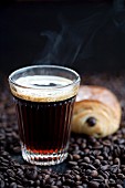 Coffee and a chocolate croissant on coffee beans