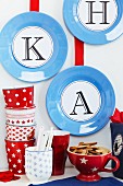 Letters stuck onto blue plates decorating wall above patterned cups and beakers