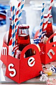 Kleine rote Papiertäschchen mit Buchstaben beklebt, darin kleine Getränkeflasche, Serviette, Strohhalme und Bonbons
