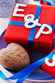Keramikbuchstaben auf roter Geschenkbox mit blauem Schleifenband und Keramikherz