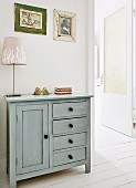 Table lamp on rustic cabinet painted pale grey next to open door in foyer