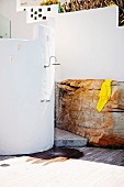 Outdoor shower on curved, white wall next to yellow towel on boulder