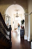 Blick vom Treppenraum durch Rundbogen auf Frau mit Hund in schmalem Gang einer herrschaftlichen Villa