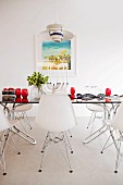 Classic, white shell chairs around glass table with red glasses in minimalist dining room