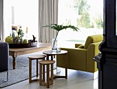 Pale wood side tables next to lime green armchair and tray of vases and ornaments on wide coffee table