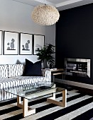 Schwarzweisser Sitzbereich im skandinavischen Stil mit Sofa und Glastisch auf Blockstreifenteppich vor anthrazitfarben getönter Kaminwand