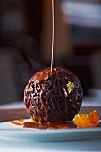An artistic chocolate ball with gold leaf and chocolate sauce