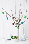 Still-life arrangement of crockery and glossy Easter eggs hanging from twigs