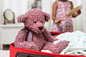 Teddybär im Koffer, im Hintergrund ein Mädchen
