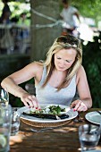 A woman eating trout with salad in a garden restaurant