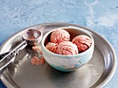 A bowl of strawberry ice cream on a tray with an ice cream scoop