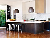 Open-plan kitchen with pendant lamps and industrial-style stools at wide breakfast bar